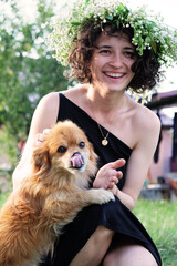 curly girl with a wreath on her head plays with a red dog