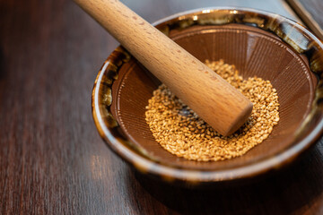 Japanese sesame grinding bowl and wooden stick. Wooden bowl with white sesame for grinding on wooden table. small stick for Japanese pork cutlet