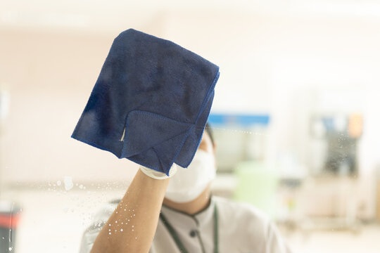 Asian woman housewife wearing rubber white gloves and holding blue cleaning clothe for wiping door glasses, cleaning up office.Woman doing housework and wipeing the glass.
