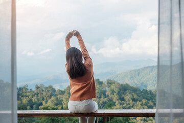 Fototapeta na wymiar Happy woman relaxing and looking mountain view at countryside home or homestay in the morning. Vacation, blogger, SoloTravel, journey, trip and relaxing concept