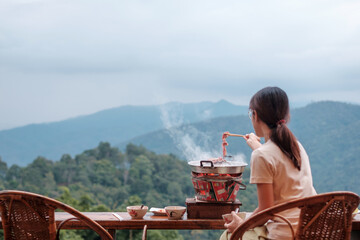 Woman grill Pork or meat with vegetables and soup on the hot pan against mountain view background, Traditional Thai BBQ style is famous in Thailand