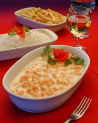 Shrimp in white cheese sauce in white bowl on red tablecloth.