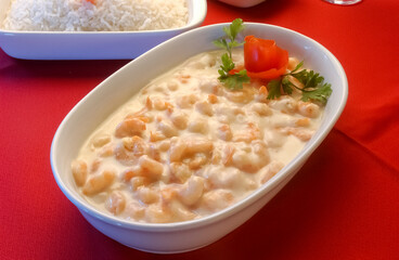Shrimp in white cheese sauce in white bowl on red tablecloth.