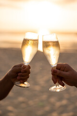 Champagne glasses cheers on the beach at sunset with sun behind