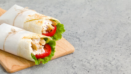 shawarma with chicken, tomatoes, sauce and lettuce on a wooden board. gray background with a place for an inscription