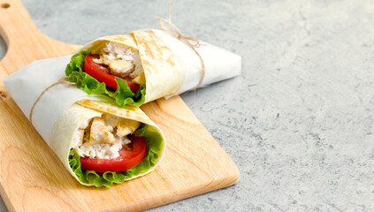 shawarma with chicken, tomatoes, sauce and lettuce on a wooden board. gray background with a place for an inscription