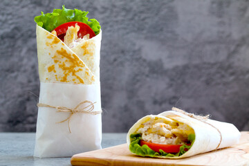 shawarma with chicken, tomatoes, sauce and lettuce on a wooden board. gray background with a place for an inscription