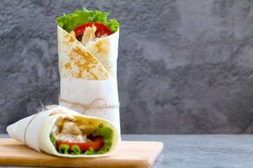 shawarma with chicken, tomatoes, sauce and lettuce on a wooden board. gray background with a place for an inscription