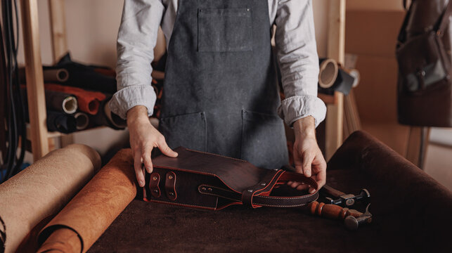 Tailor craftsman man holds handmade bag made of brown leather, handicraft production
