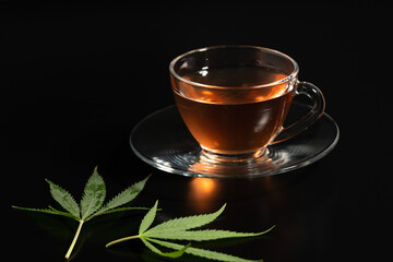 Cup with cannabis tea and marijuana leaf on black background, copy space.Herb tea for good health.