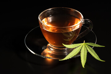 Cup with cannabis tea and marijuana leaf on black background, copy space.Herb tea for good health.