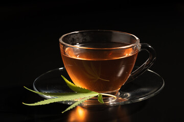 Cup with cannabis tea and marijuana leaf on black background, copy space.Herb tea for good health.