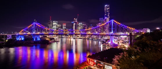 Colorful illuminated bridge and city skyline at night reflected in river © Orion Media Group
