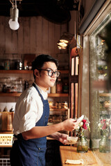 Surprised young barista looking through window after reading love note from customer on napkin