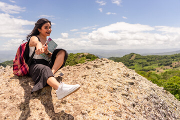 Naklejka na ściany i meble Female university student from Nicaragua smiling happy with thumb up sitting on a rock outdoors