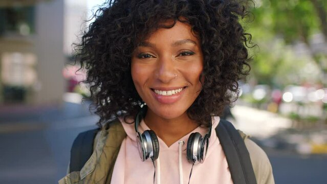 Beautiful, confident and cheerful African student smiling with curly afro hair and headphones. Portrait of a trendy young black woman with a carefree and cool attitude while traveling in the city