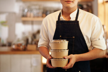 Cropped image of cafe waiter holding stack of paper container with soup or salad