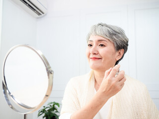 Portrait of mature aged asian woman 60s sprays perfume.