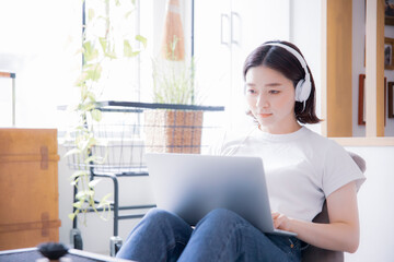 明るい室内でイヤホンとノートパソコンでオンライン授業、リモートワークをする日本人女性