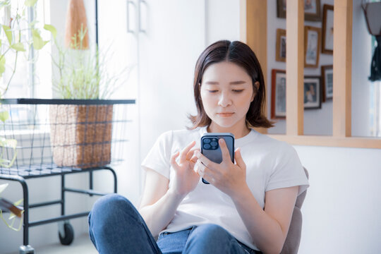 明るい室内でスマートフォンでインターネットを閲覧する日本人女性