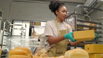 Bakery startup small business delivery. One African American female cook is packing handmade and fresh-baked bread and pastries in boxes and sending for online customer purchases in culinary kitchen.