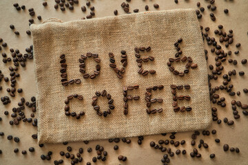 Obraz na płótnie Canvas Inscription love coffee from arabica beans on jute bag background. Mockup for coffee shop advertising in rustic style. Roasted coffee scattered on flat lay.