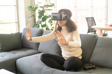 Latin woman using a virtual reality headset on sofa