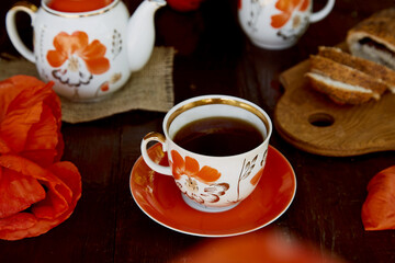 Traditional poppy seed buns, cup of black tea and milk among poppies flowers and dishes with poppies ornaments. Delicious breakfast. Summer lifestyle countryside photography