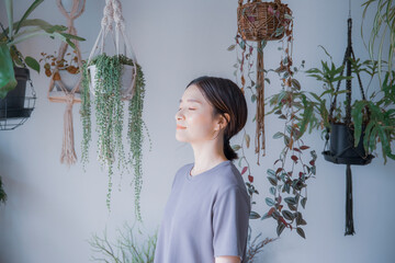 明るい植物のある室内で目を瞑るワンピース姿の日本人女性