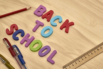 the phrase back to school is laid out in multicolored letters on the table next to colored pencils fountain pens and a ruler the concept of education school