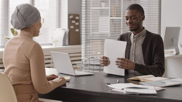 Medium slowmo of young Muslim woman and African American hr manager shaking hands after successful job interview in office