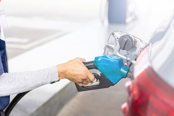 Hand of refueling worker are filling fuel to car in Petrol station. Focus on fuel nozzle and blur day light background