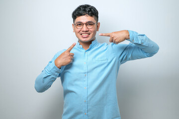 Fototapeta premium Young handsome asian man smiling cheerful showing and pointing with fingers teeth and mouth. Dental health concept.