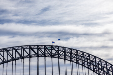 Sydney Harbour Bridge steel arch against cloudy sky with flags