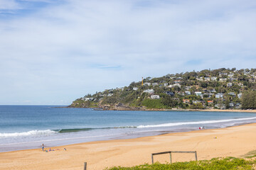 Sandy beach with clear blue water and distant headland under sunny sky