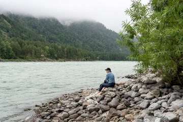 Fototapeta na wymiar the girl sits on the bank of the mountain river in rainy weather