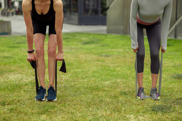 Fototapeta premium Close up of fit women trains leg muscles with fitness rubber bands in the city. Outdoor workout
