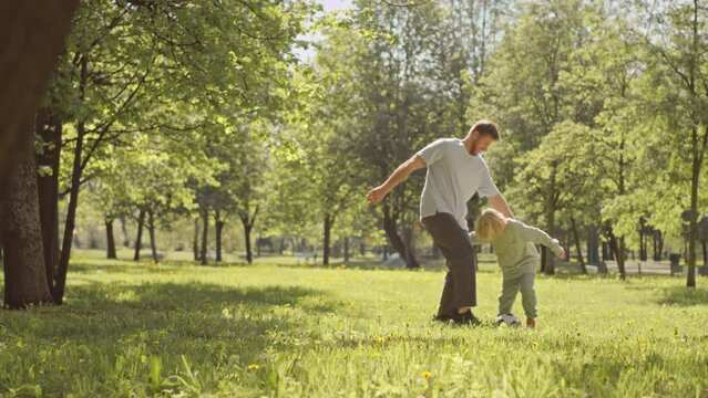 Full length slowmo of father and 7 year old son playing football on green grass in sunlight at park
