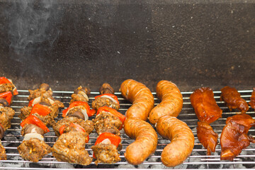 Cooking meat skewers with vegetables, sausages and steakes over the coals on barbecue grill with smoke.