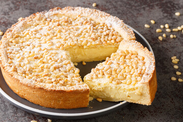 Torta della Nonna is the most delicious Italian custard tart made with sweet shortcrust pastry, custard cream and topped with pine nuts closeup in the plate on the table. Horizontal - obrazy, fototapety, plakaty