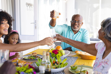 Multiracial senior man raising toast while having lunch with multigeneration family at dining table