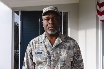African american confident military senior man in camouflage clothing and cap standing outside house