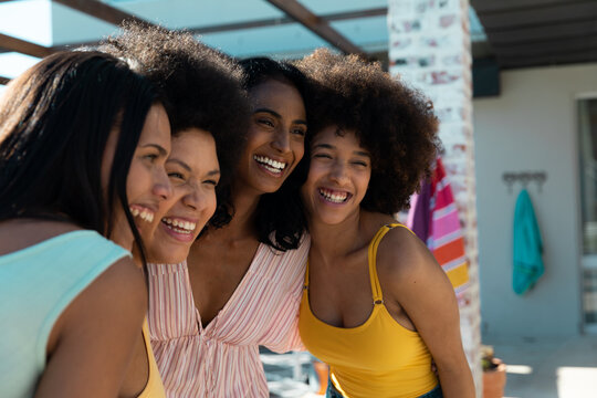 Cheerful biracial young female friends cuddling and posing while enjoying summer holiday together
