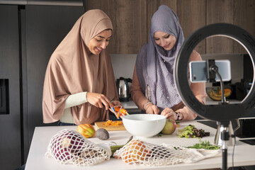 Two muslim influencers slicing, chopping and peeling vegetables at kitchen to prepare a salad.