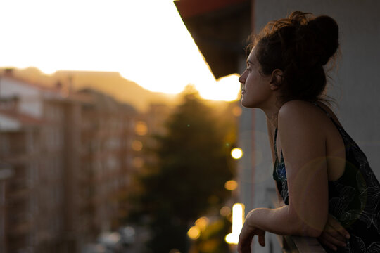 chica asom&aacute;ndose al balc&oacute;n con el atardecer de fondo