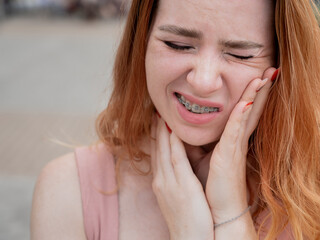 Young red-haired woman with braces suffering from pain. 