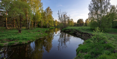 Bright May greens. Picturesque landscape with a small river. Evening pacifying landscape with a river and trees.