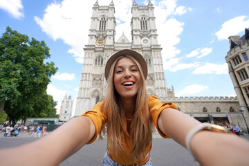 Young traveler girl taking selfie photo in London with Westminster Abbey gothic church. Young woman...
