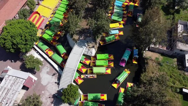 Aerial Drone Shot of colourful boats passing through Xochimilco Water Canal. Tours through water cannel with floating gardens during daytime.