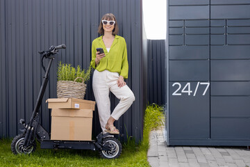 Young woman standing with phone near automatic post terminal, delivering goods by electrical...